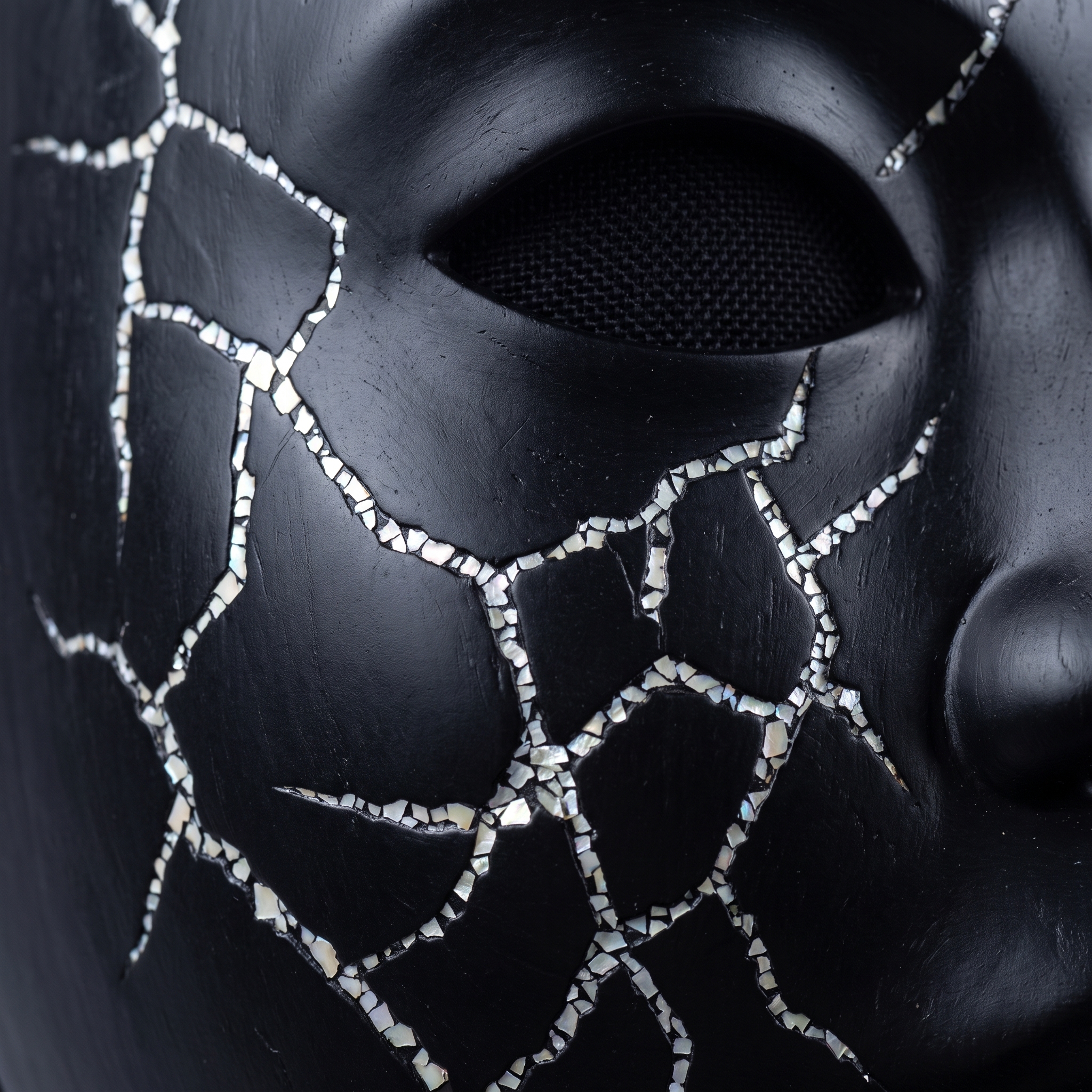 Macro photograph of a performance - extreme close-up of a black mask with cracked surface and mother-of-pearl inlay, soft diffused studio light